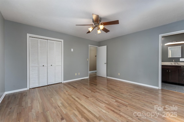 unfurnished bedroom featuring ensuite bathroom, sink, light hardwood / wood-style flooring, ceiling fan, and a closet