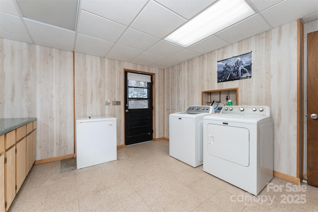 clothes washing area with cabinets, wooden walls, and washer and clothes dryer