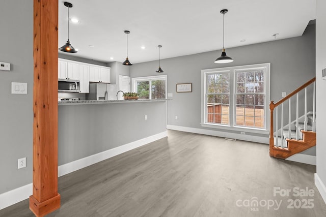 kitchen with appliances with stainless steel finishes, pendant lighting, light stone countertops, hardwood / wood-style floors, and white cabinets