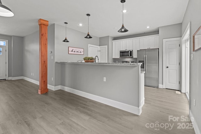 kitchen with appliances with stainless steel finishes, white cabinetry, hanging light fixtures, light hardwood / wood-style floors, and light stone countertops