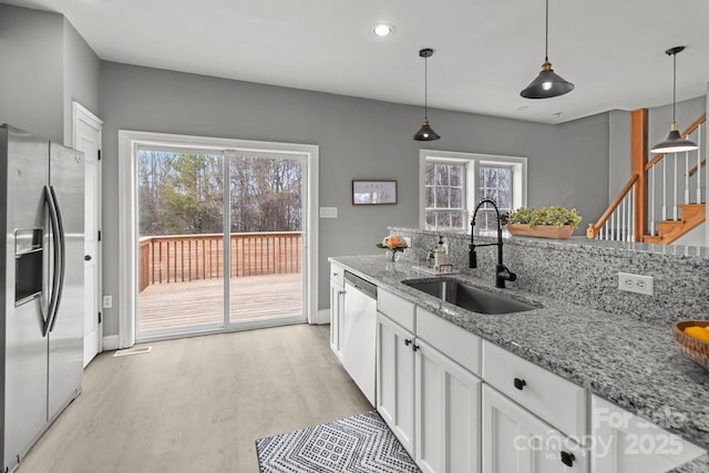 kitchen with sink, white cabinetry, hanging light fixtures, stainless steel appliances, and light stone countertops