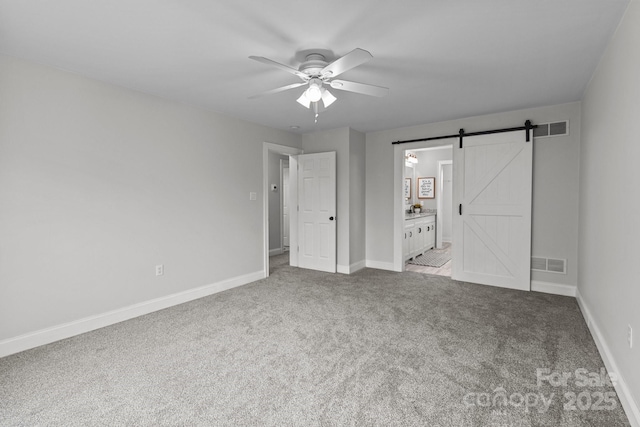 unfurnished bedroom featuring ceiling fan, connected bathroom, a barn door, and light carpet