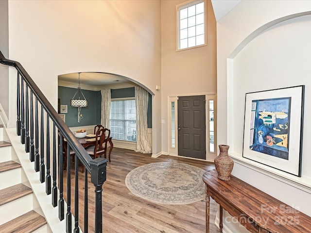 foyer entrance featuring wood-type flooring, ornamental molding, and a high ceiling