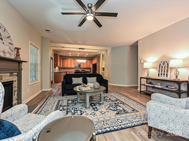 living room featuring hardwood / wood-style floors, a stone fireplace, and ceiling fan