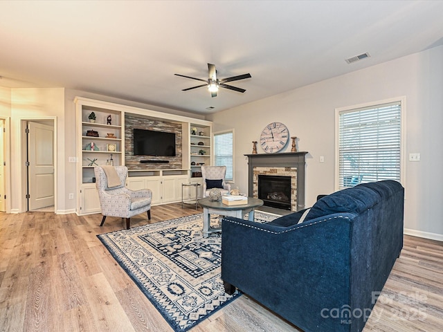 living room featuring a fireplace, built in features, ceiling fan, and light wood-type flooring