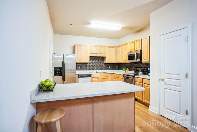 kitchen with stainless steel appliances, a kitchen bar, light brown cabinetry, and kitchen peninsula