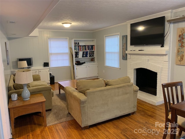 living room with crown molding, a brick fireplace, a textured ceiling, and light hardwood / wood-style floors