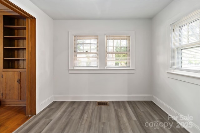 unfurnished room featuring visible vents, baseboards, and dark wood-style floors