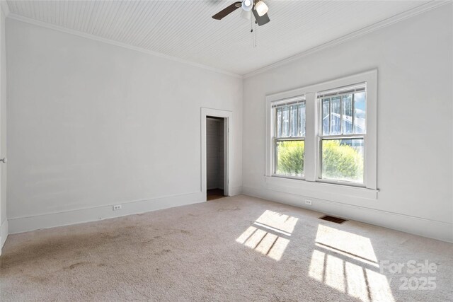 carpeted spare room with ornamental molding, baseboards, a ceiling fan, and visible vents