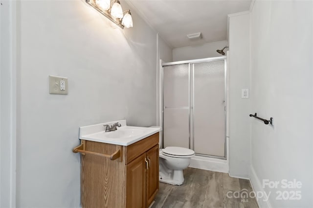 bathroom with a stall shower, vanity, toilet, and wood finished floors