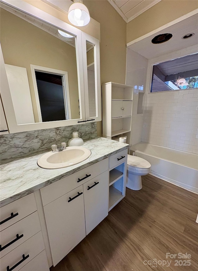 full bathroom featuring tiled shower / bath combo, vanity, wood-type flooring, ornamental molding, and toilet