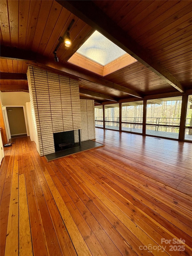 unfurnished living room with beamed ceiling, a skylight, a brick fireplace, wooden ceiling, and hardwood / wood-style flooring