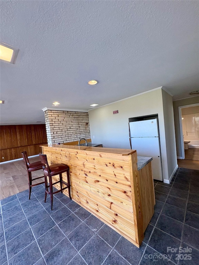 bar with ornamental molding, white fridge, wooden walls, and a textured ceiling