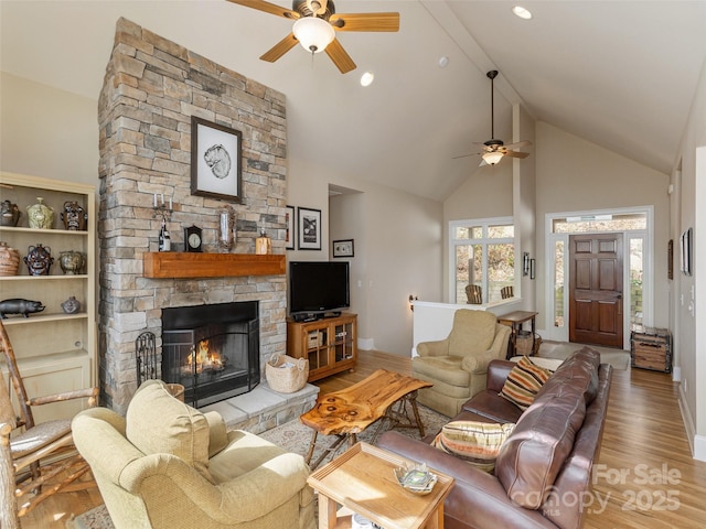 living room featuring ceiling fan, a stone fireplace, high vaulted ceiling, and light wood-type flooring