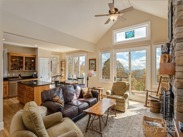 living room featuring ceiling fan, high vaulted ceiling, a fireplace, and light hardwood / wood-style floors