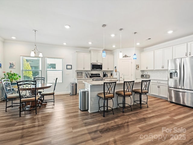 kitchen featuring a breakfast bar, white cabinetry, hanging light fixtures, stainless steel appliances, and a center island with sink