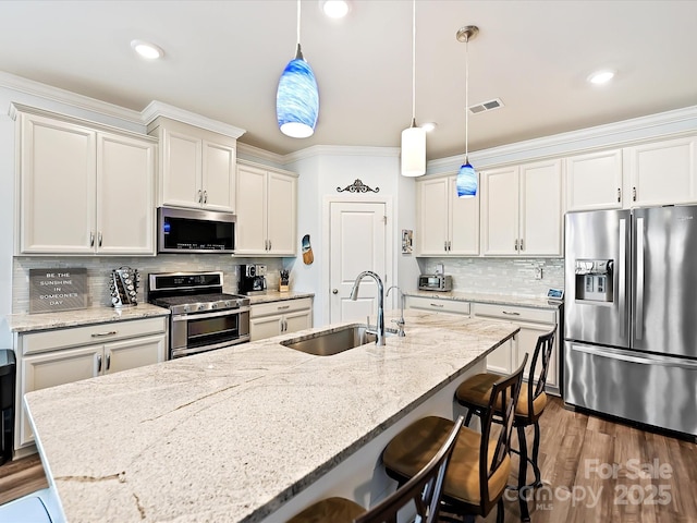 kitchen featuring sink, hanging light fixtures, a center island with sink, appliances with stainless steel finishes, and a kitchen breakfast bar