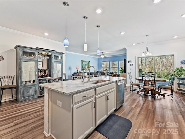 kitchen featuring pendant lighting, sink, a kitchen island with sink, stainless steel dishwasher, and light stone countertops