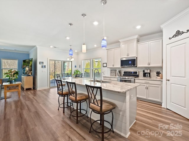 kitchen featuring white cabinetry, stainless steel appliances, an island with sink, and hanging light fixtures