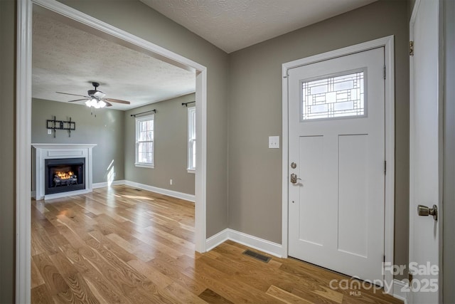 foyer entrance with ceiling fan, light wood-type flooring, and a textured ceiling