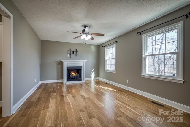 unfurnished living room featuring ceiling fan, light hardwood / wood-style floors, and a textured ceiling