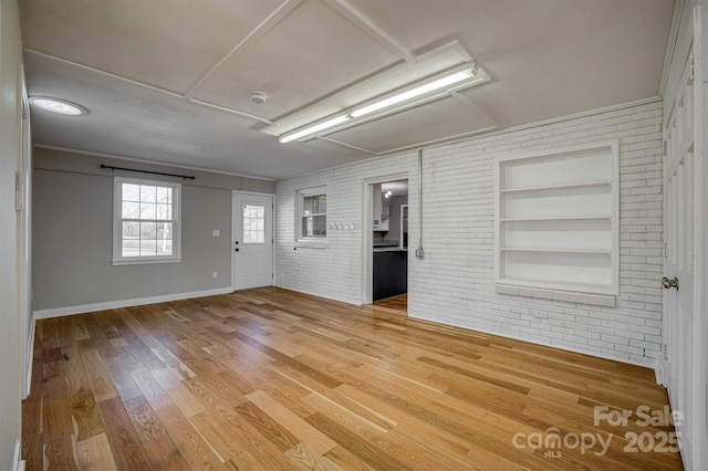 empty room with built in shelves, brick wall, and hardwood / wood-style floors