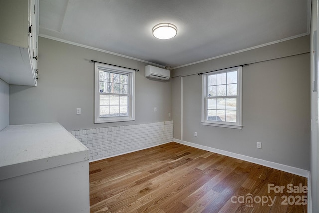 empty room featuring a healthy amount of sunlight, a wall mounted air conditioner, light hardwood / wood-style flooring, and ornamental molding