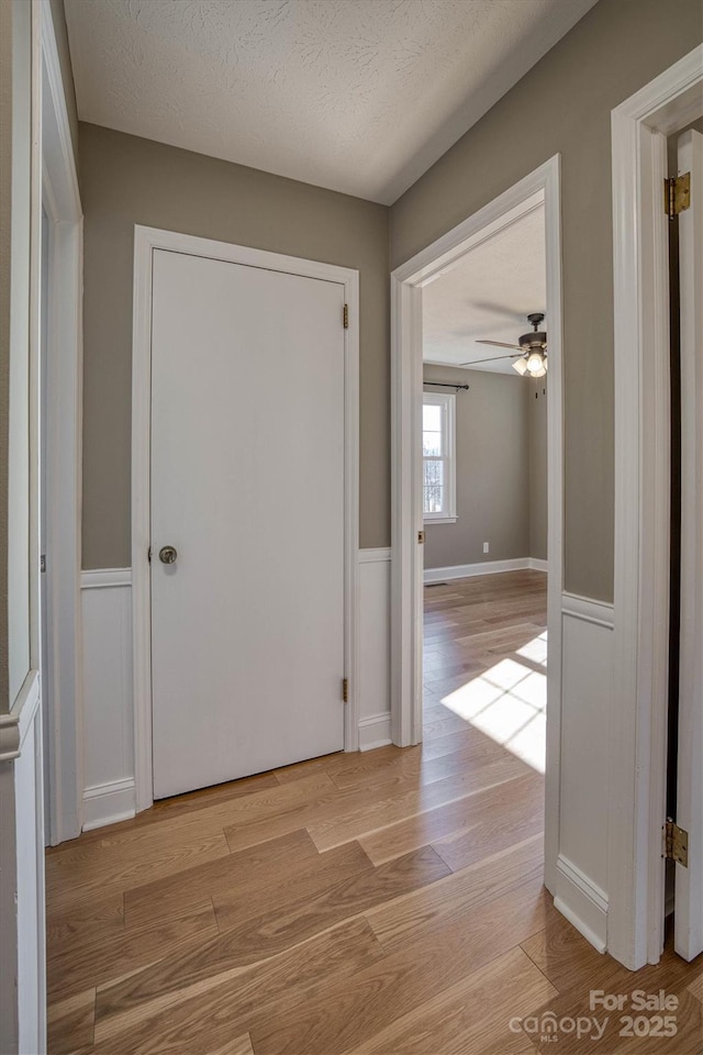 hall with a textured ceiling and light hardwood / wood-style floors