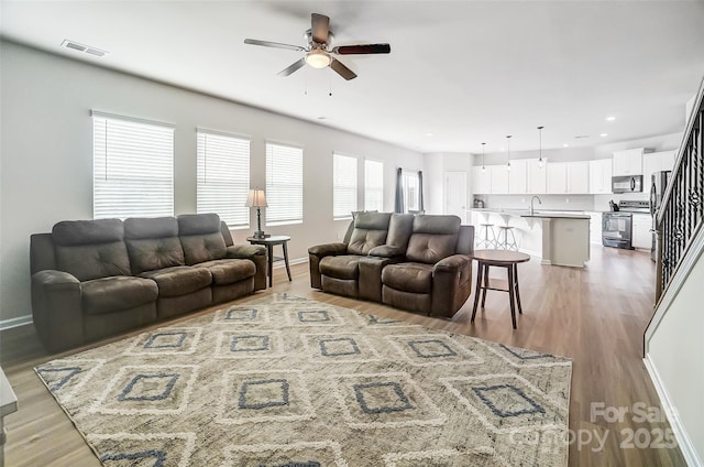 living room with ceiling fan, sink, and light wood-type flooring