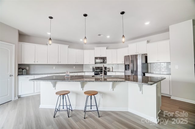 kitchen with a breakfast bar, an island with sink, dark stone countertops, white cabinets, and stainless steel appliances