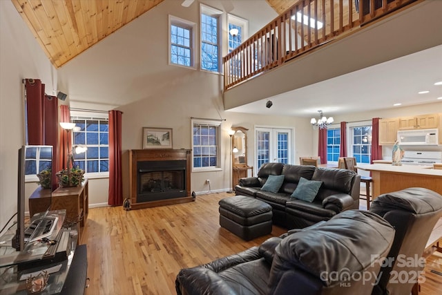 living room featuring french doors, high vaulted ceiling, light hardwood / wood-style floors, and a notable chandelier