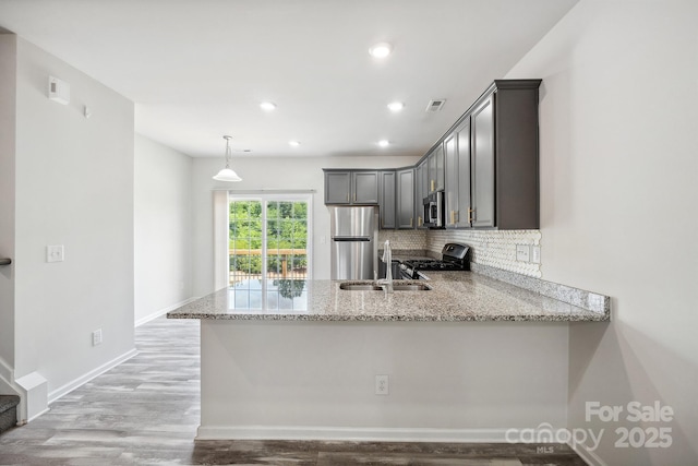 kitchen with appliances with stainless steel finishes, decorative backsplash, hanging light fixtures, kitchen peninsula, and light stone countertops