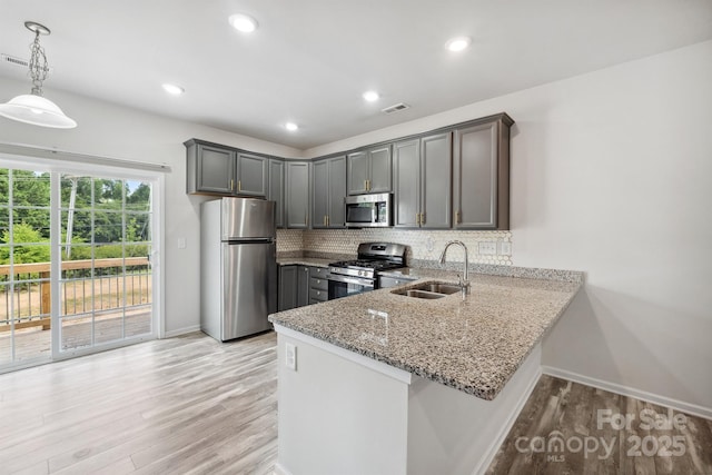 kitchen featuring sink, appliances with stainless steel finishes, decorative backsplash, decorative light fixtures, and kitchen peninsula