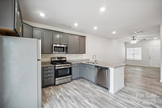 kitchen featuring light stone counters, stainless steel appliances, gray cabinets, and sink