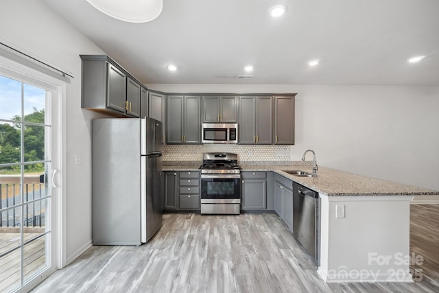 kitchen with gray cabinets, appliances with stainless steel finishes, sink, kitchen peninsula, and light stone countertops