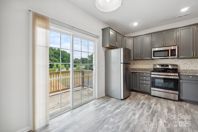 kitchen with appliances with stainless steel finishes, gray cabinets, decorative backsplash, and light hardwood / wood-style flooring