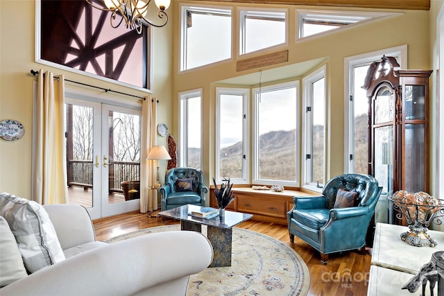 living room featuring hardwood / wood-style floors, a chandelier, a high ceiling, a mountain view, and french doors