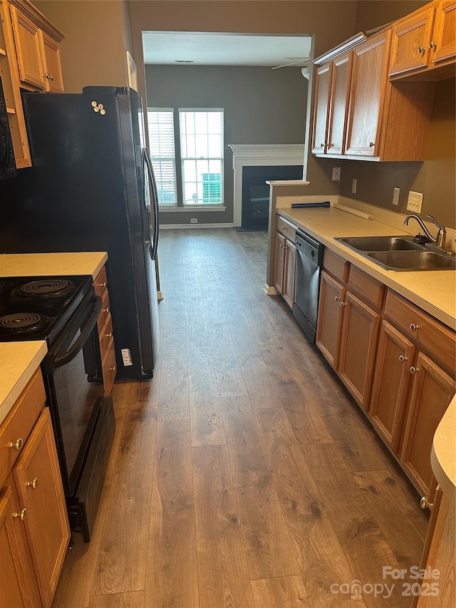 kitchen featuring dishwashing machine, dark wood-style floors, brown cabinetry, a sink, and black range with electric cooktop