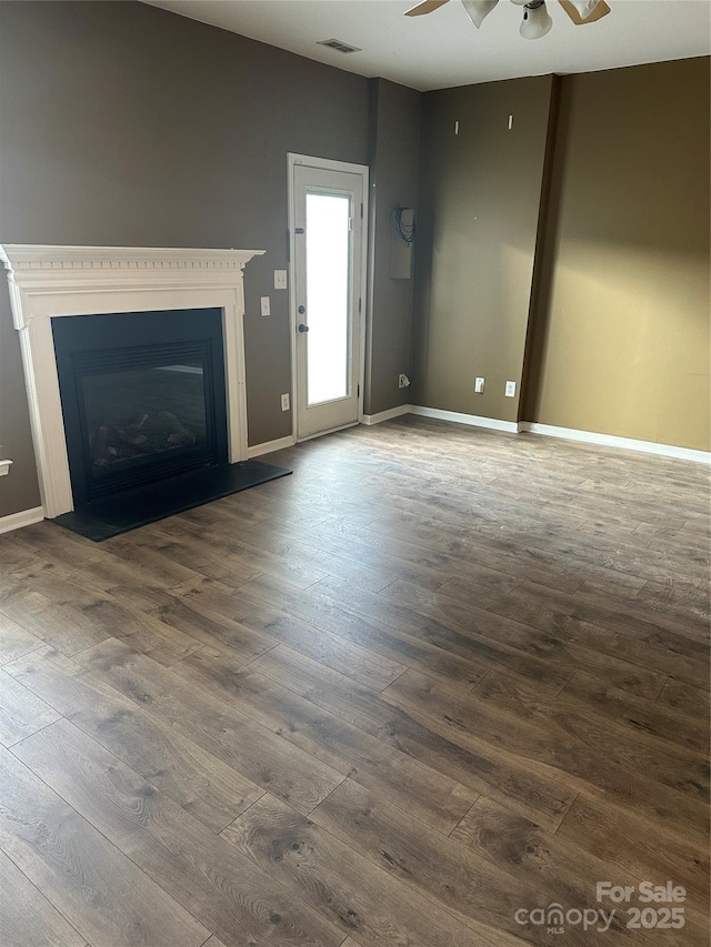 unfurnished living room with wood finished floors, a ceiling fan, visible vents, baseboards, and a fireplace