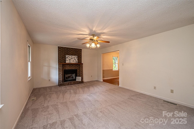 unfurnished living room with ceiling fan, light colored carpet, a fireplace, and a textured ceiling