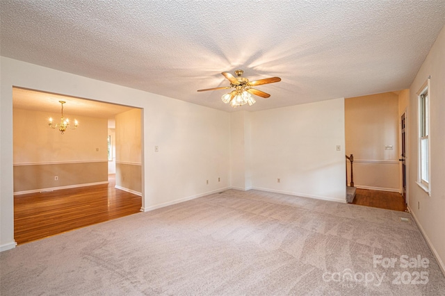 carpeted spare room featuring ceiling fan with notable chandelier and a textured ceiling