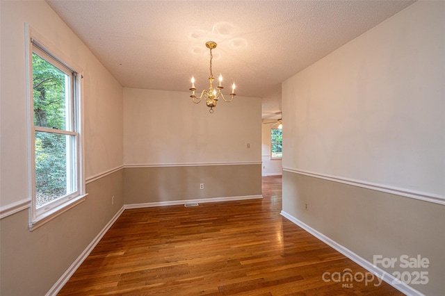 empty room featuring dark hardwood / wood-style flooring, a textured ceiling, a wealth of natural light, and a chandelier