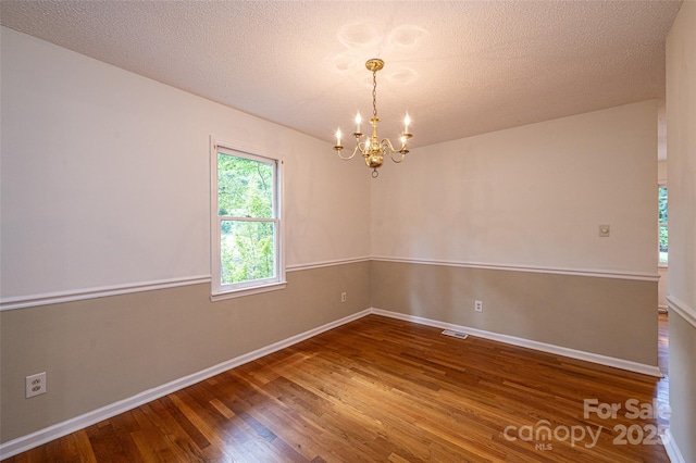 empty room featuring wood-type flooring, a textured ceiling, and a chandelier