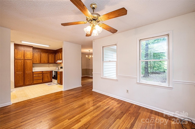 unfurnished living room featuring built in desk, ceiling fan with notable chandelier, a textured ceiling, and light wood-type flooring