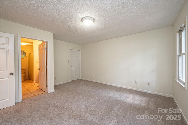 unfurnished bedroom with light colored carpet, connected bathroom, multiple windows, and a textured ceiling