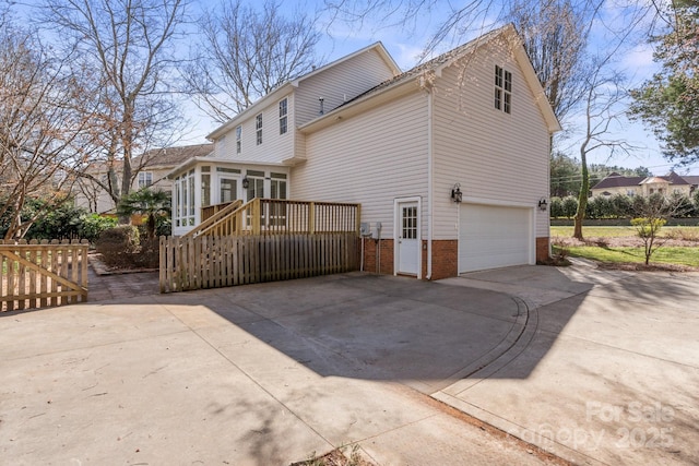 rear view of property featuring brick siding, driveway, a garage, and a sunroom