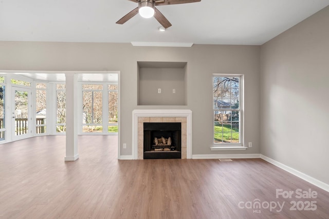 unfurnished living room with wood finished floors, visible vents, baseboards, ceiling fan, and a tiled fireplace