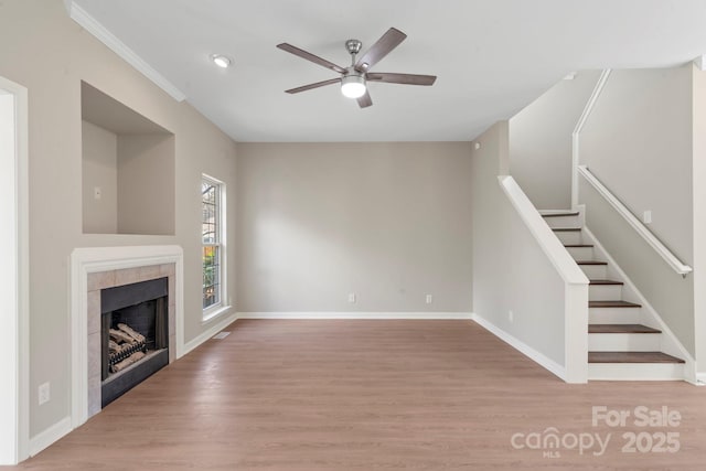 unfurnished living room featuring baseboards, wood finished floors, ceiling fan, and a tile fireplace