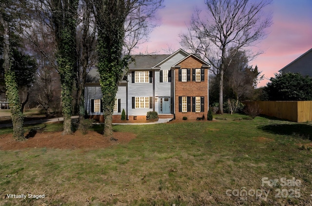 colonial inspired home featuring brick siding, a front yard, and fence