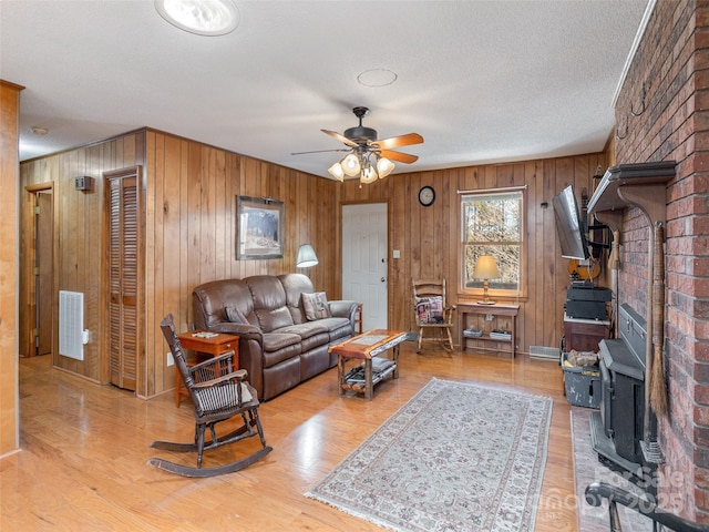 living room featuring a textured ceiling, light hardwood / wood-style floors, ceiling fan, and a wood stove